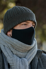 A Shallow focus of an adult caucásico male wearing a facemask, with a knitted scarf and winter hat, in a park