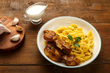 Light plate of pasta in a creamy sauce with cheese and chicken on the table next to garlic and cream on stands.