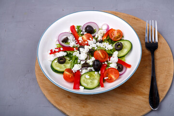 Light plate of Greek salad on a round shelf with a fork on a concrete background.