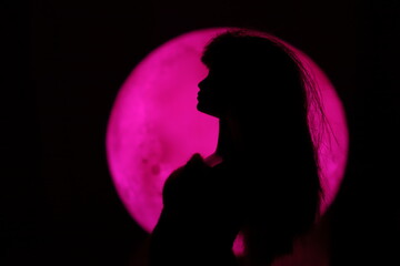 A female doll silhouette in the night in front of a circular light source with space to write your text 
