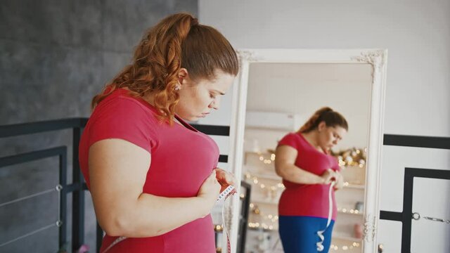 Young plus size lady measuring waist with tape, disappointed because of big result