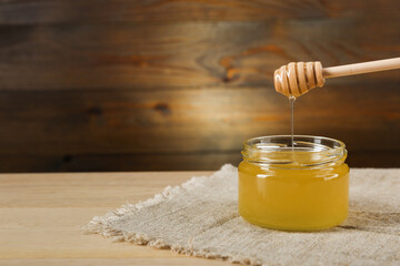 honey flowing from honey dipper into the jar on wooden background in rustic style