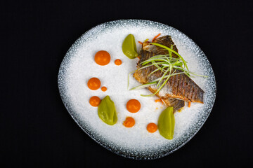 Tuna steak covered with broccoli and decorations on white plate and black background
