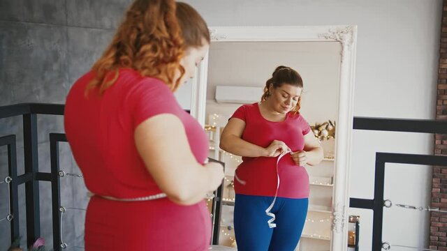 Young overweight woman feeling happy after measuring her waist at home