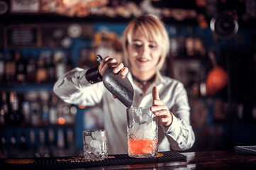 Portrait of girl barman places the finishing touches on a drink in the bar