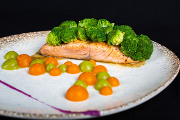 Tuna steak covered with broccoli and decorations on white plate and black background