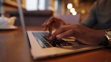 African-American male fingers working by laptop keyboard in a cafe
