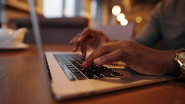African-American male fingers working by laptop keyboard in a cafe