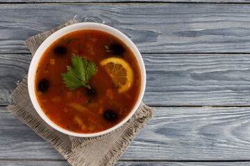 Solyanka soup with meat, sausage, vegetables, olives and lemon in a plate.
