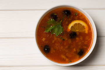 Solyanka soup with meat, sausage, vegetables, olives and lemon in a plate.