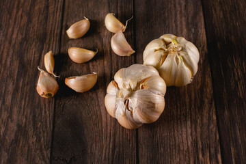 Heads of garlic lying on a dark wooden surface, along with cloves of garlic used to season the food.