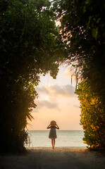 Elegant woman standing under natural arch, Maldives.