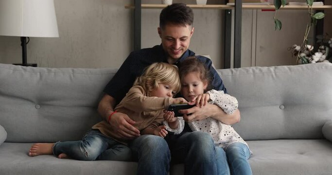 Dad sit on couch with preschool son and daughter using smartphone, having fun spend time on internet, prefer using cellphone instead of live communication, addition, gadget overuse, bad habit concept
