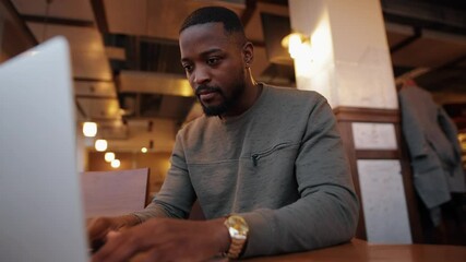 Serious African American man opening laptop and working sitting in a cafe - Powered by Adobe