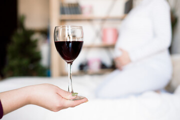 Pregnant woman keeping glass of wine. Future mother drinking alcohol while expecting little baby. Concept of unhealthy lifestyle and harmfulness.
