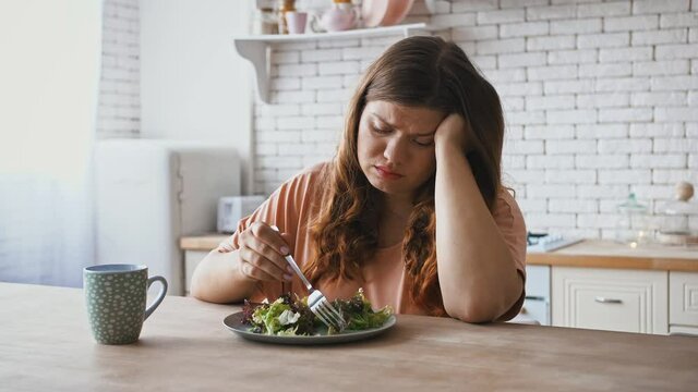 Plus size woman sitting at table, feeling unhappy with diet not wanting to eat salad