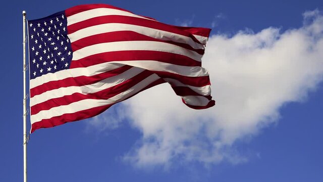 American flag waving against blue sky and white clouds.