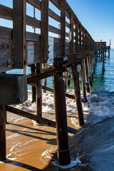 Balboa Pier in Newport Beach, CA, with water swirling beneath the pier. Built in 1906, the pier's wooden pillars weren't reinforced with steel sheathing and braces until after storm damage in 1998.