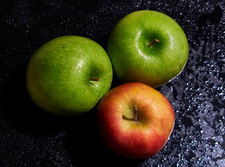 three red and green apples on wet black background
