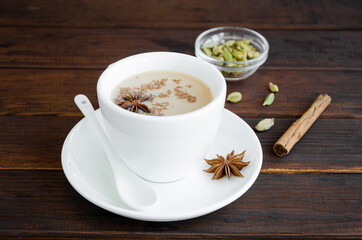 Hot tea with milk, cinnamon, cardamom, anise and other spices, Indian masala tea in a white cup on a wooden background. copy space.