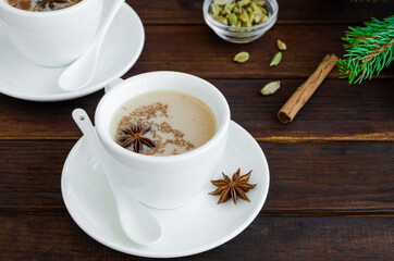 Hot tea with milk, cinnamon, cardamom, anise and other spices, Indian masala tea in a white cup on a wooden background. copy space.