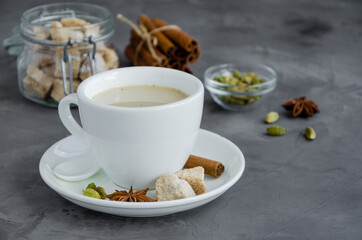Hot tea with milk, cinnamon, cardamom, anise and other spices, Indian masala tea in a white cup on a dark background. copy space.