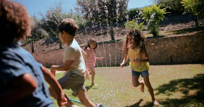 Group of children playing and jumping over sprinkler on garden