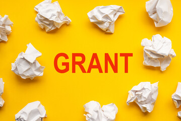 Grant text on yellow background with copy space. Crumpled sheets of paper lie around. Business concept image