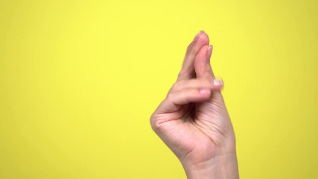 Closeup view 4k video of female manicured beautiful hand snapping her fingers happily and cheerfully. Hand of woman isolated on yellow bright background.