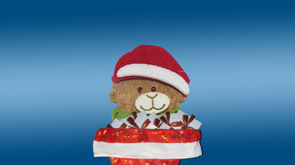 Bear in a red cap of Santa Claus with gifts on a blue background.
