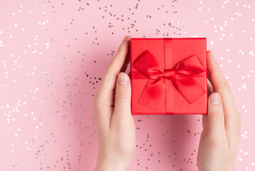 Getting present concept. Top above overhead close up view photo of female hands holding small cute giftbox over pasle pink background with silver glitter