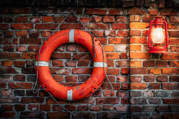 Old, grungy and weathered lifebuoy and red vintage lit oil lamp on rustic red and brown brick wall....