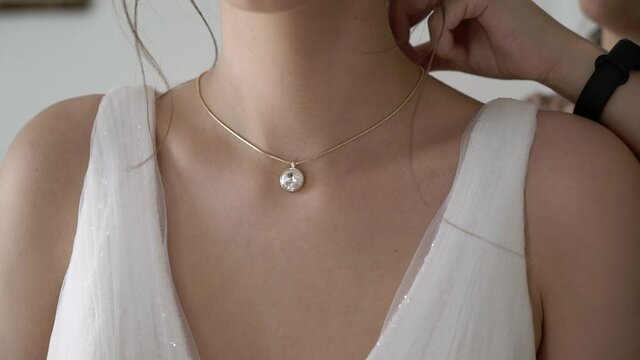 Bridesmaid helping to wear necklace for bride. Wedding morning dressing