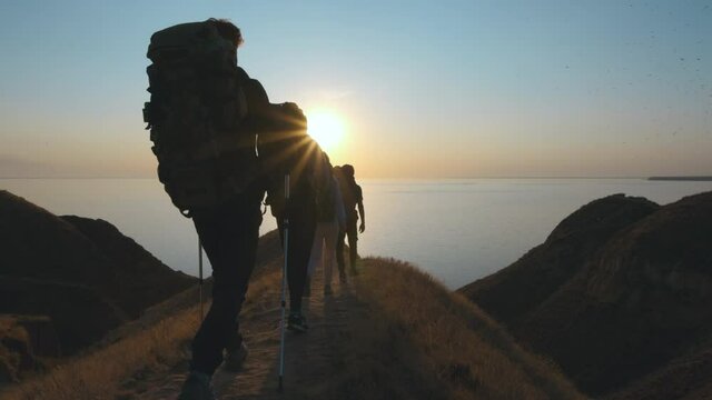 The tourists with backpacks walking on the mountain near the sea. slow motion