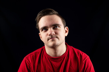 Fototapeta premium Young man in casual t-shirt standing against isolated dark background