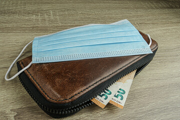 Is a brown leather wallet with euro bills on top is a blue medical mask