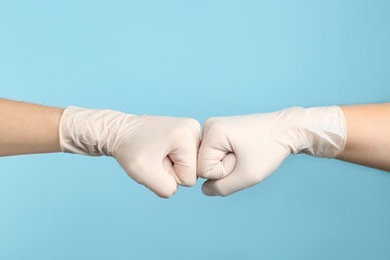 People in medical gloves doing fist bump on light blue background, closeup of hands