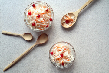 Sauerkraut with cranberry berries on a gray background, wooden spoons, top view-the concept of cooking delicious dishes from vitamin vegetables