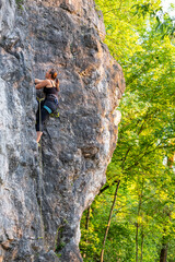happy beautiful caucasian woman with long brown hair rock climbing, flexing her muscles on a sunny day in the mountains, strongly holding on to cliffs. Healthy outdoor sports and activities in nature