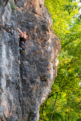 happy beautiful caucasian woman with long brown hair rock climbing, flexing her muscles on a sunny day in the mountains, strongly holding on to cliffs. Healthy outdoor sports and activities in nature