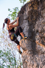 happy beautiful caucasian woman with long brown hair rock climbing, flexing her muscles on a sunny day in the mountains, strongly holding on to cliffs. Healthy outdoor sports and activities in nature
