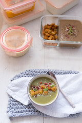 Overhead view of some batch cooking glass jars full of food and a bowl of creamy zucchini soup at the bottom.