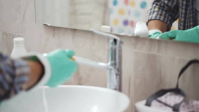 Close up of aged man in gloves with sponge doing bathroom cleaning