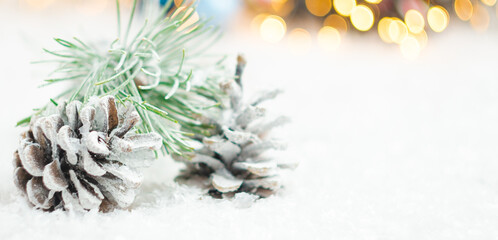 Pine cones and spruce branch covered with snow on the background of blurred lights of garland. Christmas concept with copy space.