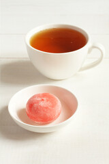 Pomegranate with honey Japanese dessert mochi on a white saucer and a cup of green tea on a white wooden table. Closeup