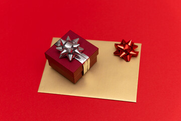 a gift red box with a silver bow stands on a gold envelope. red background