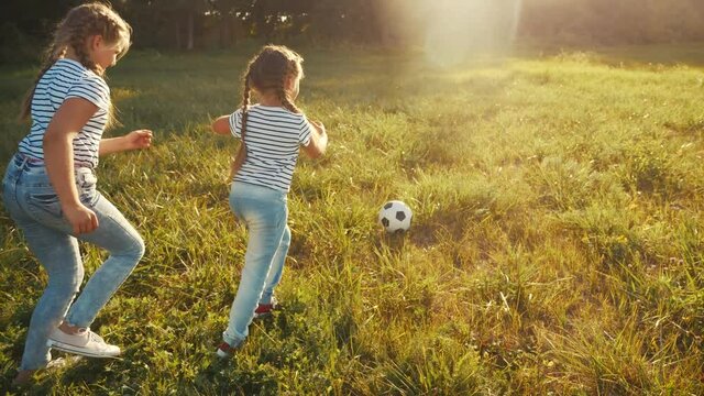 two little girls play soccer in the park with a ball. kid dream concept. kid play ball on green grass in the park. child playing soccer. people in the park fun concept