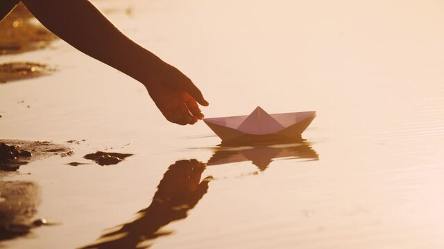 child puts a paper boat into the water. happy family fantasy kid dream concept. child playing with paper boat ship. a child hand launches a boat in lifestyle a park in a pond