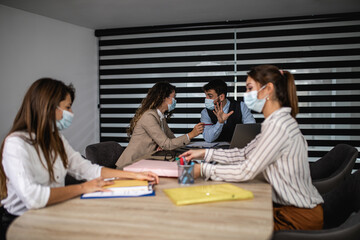 Group of four business people working together are talking and analyzing their business plan. They wearing protective face masks against virus infection.