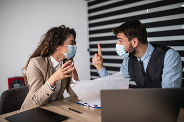 Serious business partners or colleagues sitting in office and talking about job problems caused by Covid-19 pandemic. They wearing protective face masks.